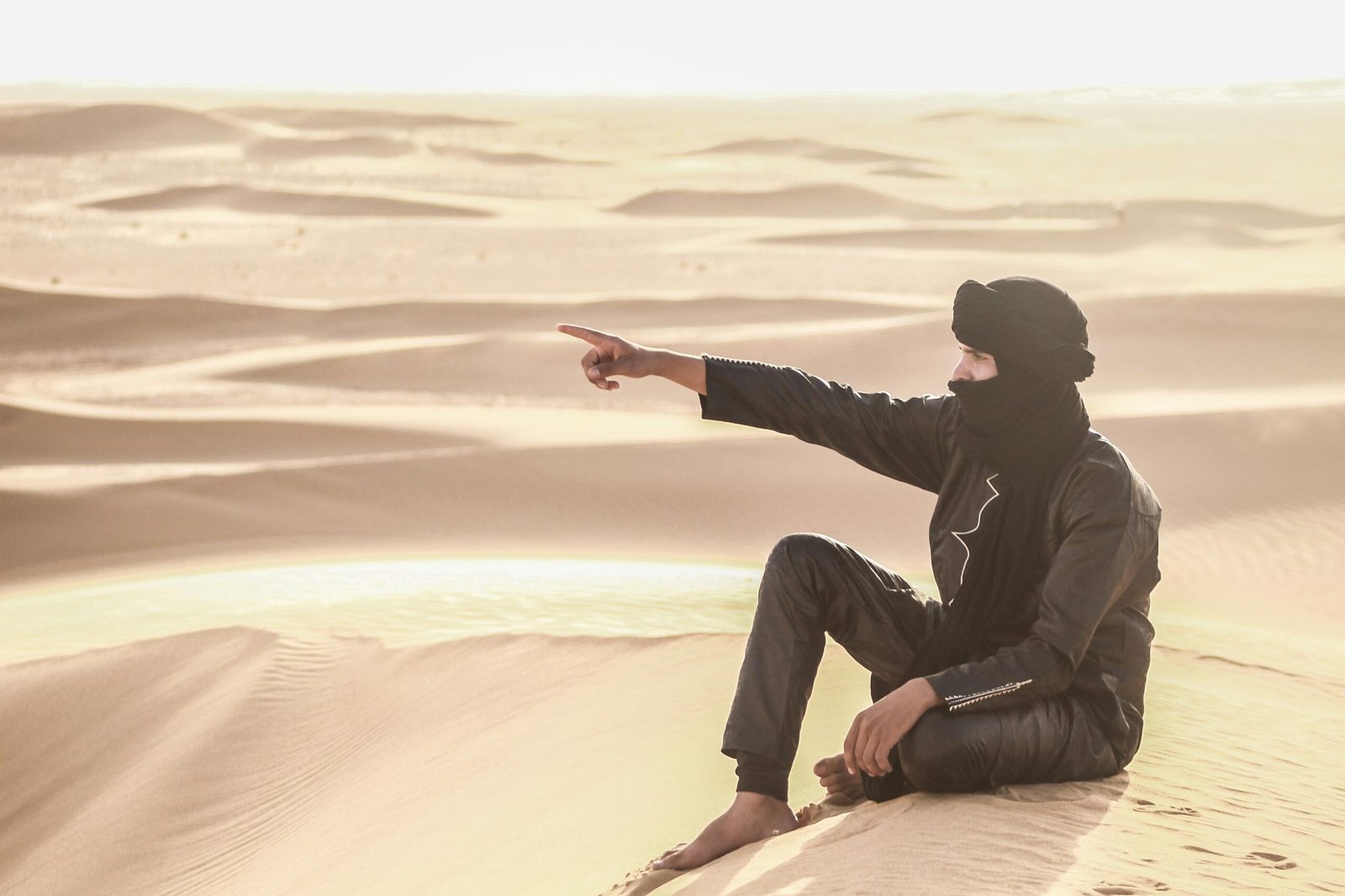 Man in traditional attire pointing across dunes in the Sahara Desert.