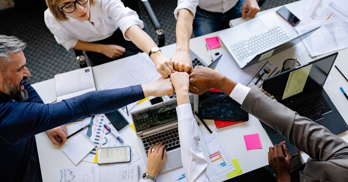 Creative team unites with a fist bump signifying collaboration in an office setting.